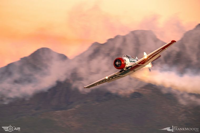 Harvard trailing smoke past mountains at sunset, air-to-air photograph by Frank Moody